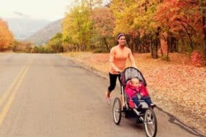 woman postpartum running pushing a stroller on a road with autumn trees on the side